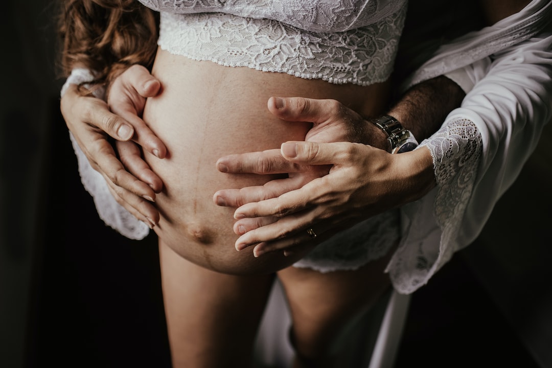 Pregnant person being held by another person arms wrapped from behind around belly. 